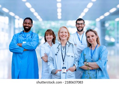 Diverse Group Of Doctors And Nurses In Hospital Clinic. Smiling Friendly Health Care Workers Looking At Camera While Standing In Bright Modern Corridor. Multiethnic Medical Staff Portrait