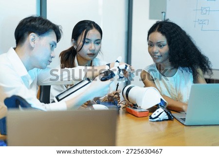 Diverse group of engineering students collaborating on robotic technology in modern laboratory. Multicultural team developing robotics, artificial intelligence, and innovation concepts using laptop, electronic components, and robotic arm prototype.