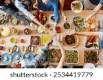 A diverse group enjoying a meal together, sharing food and drinks. Top view of a table with various dishes, showing a sense of community and celebration. Diverse people celebrating and toasting.