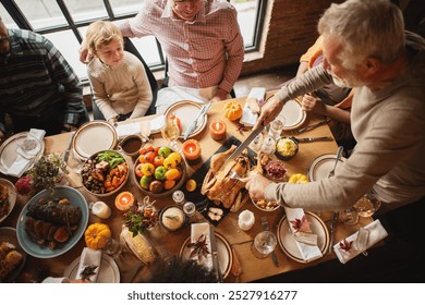 A diverse group enjoys a Thanksgiving meal. A man carves turkey at a table filled with food, candles, and autumn decor. Family and friends gather for a holiday feast. Family celebrating Thanksgiving. - Powered by Shutterstock