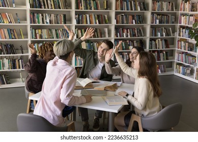 Diverse group of excited students enjoying teamwork, education process in college library, giving team high five, clapping hands, laughing, sitting together at table with open books - Powered by Shutterstock