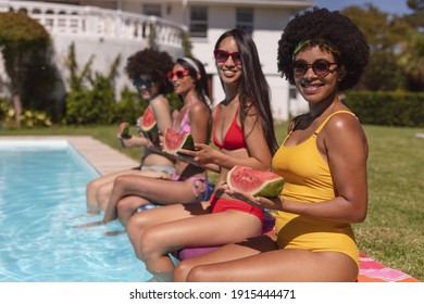 Diverse Group Of Female Friends Eating Watermelon Sitting At The Poolside Talking. Hanging Out And Relaxing Outdoors In Summer.