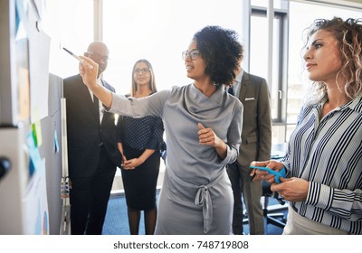 Diverse group of focused businesspeople brainstorming together on a whiteboard during a strategy session in a bright modern office - Shutterstock ID 748719808