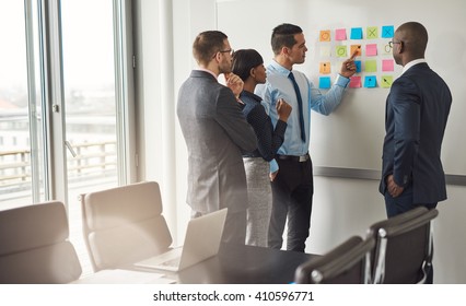 Diverse Group Of Four Business People Gathered Around White Board With Sticky Notes Planning Something