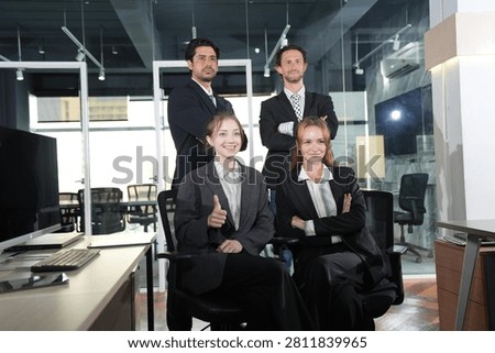 A diverse group of four professionals poses together, the standing men and seated women exchanging warm smiles in a glass-walled night office in a bright modern coworking office.