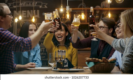 Diverse Group of Friends Celebrate with a Toast and Clink Raised Glasses with Various Drinks in Celebration. Beautiful Young People Have Fun in the Stylish Bar/ Restaurant.