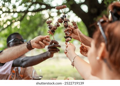 Diverse group of friends celebrating with grilled meat skewers at an outdoor barbecue. Multicultural gathering in nature, showcasing unity, food sharing, and summer lifestyle. - Powered by Shutterstock