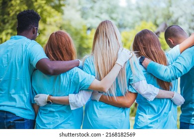 Diverse Group Of Friends Cleanup A Park During A Charity Event. They Are Standing With Their Arms Around One Another.
