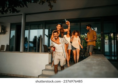 Diverse group of friends embracing the warmth of the setting sun, laughing and toasting to good times in a vibrant house yard gathering - Powered by Shutterstock