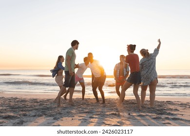 Diverse group of friends enjoy a beach outing at sunset. Laughter fills the air as they share a playful moment by the sea. - Powered by Shutterstock