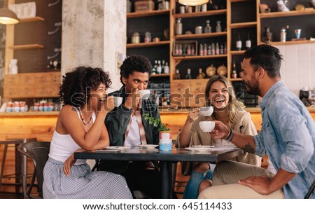 Diverse group of friends enjoying some coffee together in a restaurant and talking. Young people sitting around cafe table and drinking coffee.