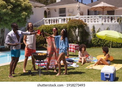 Diverse Group Of Friends Having Barbecue And Talking At A Pool Party. Hanging Out, Drinking Beer, Making A Toast And Relaxing Outdoors In Summer.