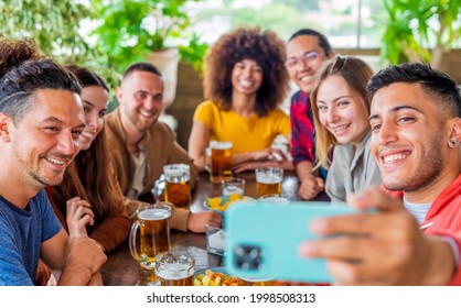 diverse group of friends making a selfie celebrating happy hour with beers and food in a bar restaurant. multiethnic people having fun in a party together smiling at the camera. self portrait concept - Powered by Shutterstock