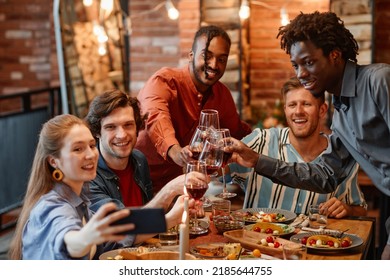 Diverse Group Of Friends Taking Selfie Photo At Table During Dinner Party And Clinking Glasses