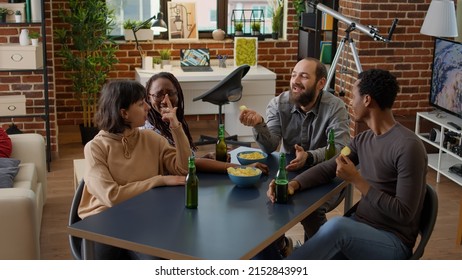 Diverse group of friends talking and having fun in living room, drinking beer and eating chips. Happy people having conversation at leisure activity gathering, enjoying discussion together. - Powered by Shutterstock