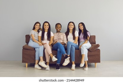 Diverse Group Of Happy Attractive Women Sitting On Couch, Looking At Camera And Smiling. Cheerful Beautiful Young Mixed Race Female Friends Hanging Out Together, Relaxing On Sofa And Having Good Time