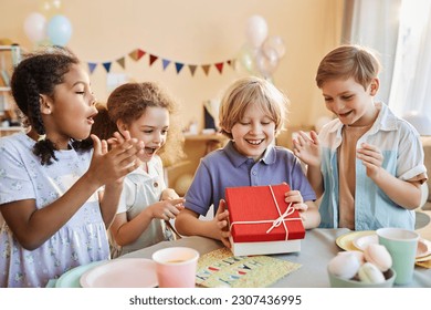 Diverse group of happy children at Birthday party with excited boy opening presents - Powered by Shutterstock