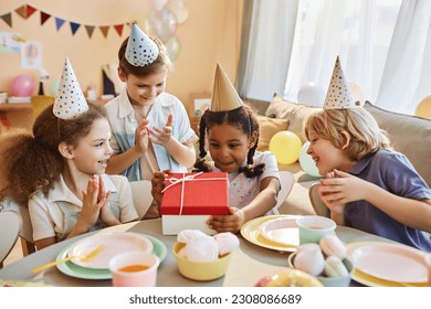 Diverse group of happy children at Birthday party with little black girl opening presents - Powered by Shutterstock