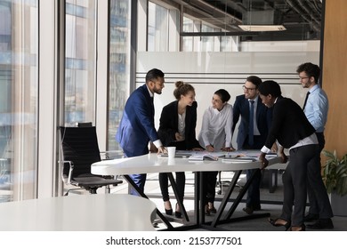 Diverse group of happy employees analyzing reports together, standing at table with papers, working together, discussing marketing, statistic data, talking, brainstorming. Business meeting concept - Powered by Shutterstock