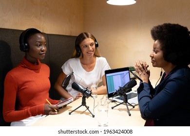 Diverse group of happy female business colleagues wearing headphones, speaking to microphones. recording podcast and business in a modern office. - Powered by Shutterstock