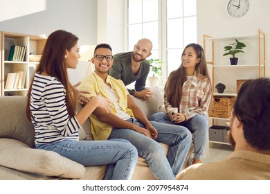 Diverse group of happy young friends having fun together. Smiling mixed race multi ethnic people talking and sharing interesting stories while sitting on the sofa at a friendly get-together at home - Powered by Shutterstock