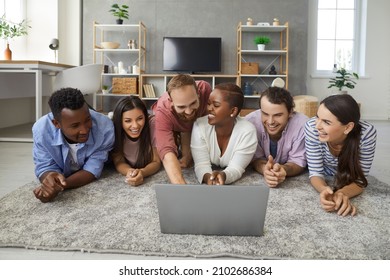 Diverse Group Of Happy Young Multiracial College Students And Friends Having Friendly Gathering At Home, Lying Together On Floor In Living Room, Watching Funny Movie Or TV Show On Laptop And Laughing