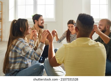 Diverse Group Of Happy Young People Having Fun Time Together. Cheerful Mixed Race Friends Sitting In Circle On Floor At Home, Holding Hands And Laughing At Funny Joke. Community And Friendship Concept