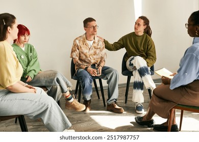 Diverse group of individuals engaging in group therapy session, listening and participating in an informal setting with bright flooring and relaxed atmosphere - Powered by Shutterstock