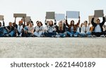 A diverse group of individuals, seated on the pavement, participate in a peaceful protest for climate action. They hold blank signs, symbolizing unity, advocacy, and the demand for change.