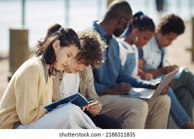 Diverse Group Of Kids Sitting In Row And Writing In Notebooks Outdoors During Summer School Lesson