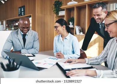 Diverse group of laughing businesspeople reading graphs and paperwork together during a meeting at a boardroom table in an office - Shutterstock ID 1528892327