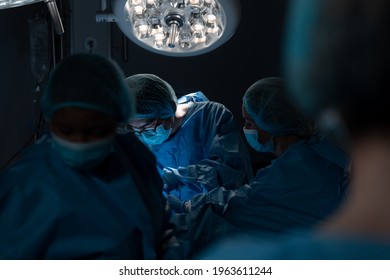 Diverse Group Of Male And Female Surgeons In Operating Theatre Wearing Face Masks Performing Surgery. Medicine, Health And Healthcare Services During Coronavirus Covid 19 Pandemic.