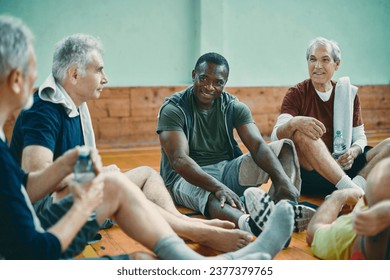 Diverse group of male senior friends sitting on the floor of a gym after playing basketball - Powered by Shutterstock