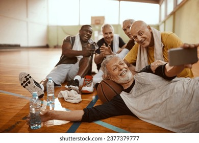 Diverse group of male senior friends taking selfies after playing basketball in a indoor gym - Powered by Shutterstock