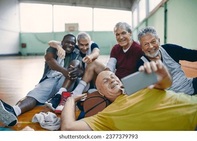 Diverse group of male senior friends taking selfies after playing basketball in a indoor gym - Powered by Shutterstock