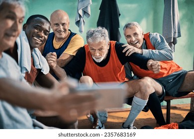 Diverse group of male seniors taking a selfie on a smartphone in the locker room after playing football - Powered by Shutterstock