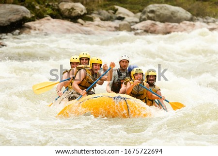 A diverse group of men and women in Ecuador rowing a white water raft through challenging rapids, working together as a team for an extreme sport adventure.