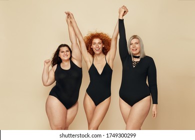 Diverse. Group Of Models With Different Figure And Size Portrait. Smiling Blonde, Brunette And Redhead In Black Bodysuits Holding Hands Up. Female Friendship For Happy Life. 