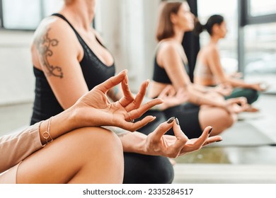 diverse group of multiethnic female friends meditating in easy pose with gyan mudra gesture while practicing yoga in gym, blurred background, harmony and wellness concept - Powered by Shutterstock