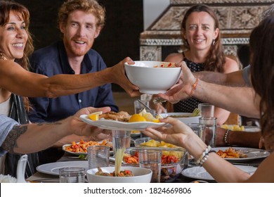 Diverse group of multiethnic friends enjoying meal sharing and passing food to each other in outdoor cafe or home. Leisure, eating, food and drinks, people and holidays concept