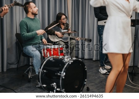 A diverse group of musicians practices instruments passionately in a studio environment. The group consists of a drummer, a guitarist, and a singer, evoking creativity, concentration, and teamwork.