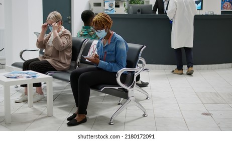 Diverse Group Of Patients With Face Masks Sitting In Waiting Area At Hospital Reception, Preparing To Start Medical Checkup Appointment During Covid 19 Pandemic. Healthcare Exam.