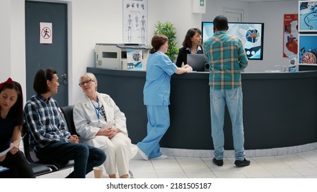 Diverse Group Of Patients Sitting In Waiting Room Area To Register For Appointment, Waiting To Start Consultation At Hospital Reception Desk. Sick People In Clinic Lobby To Do Checkup Visit.