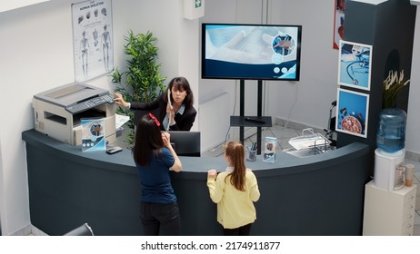 Diverse Group Of Patients Waiting To Attend Medical Appointment, Sitting At Busy Hospital Reception Desk. People With Healthcacare Insurance Having Examination With Specialist. Handheld Shot.