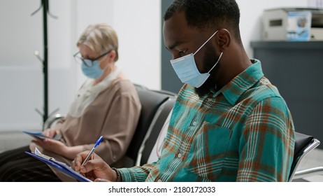 Diverse Group Of People With Face Masks In Waiting Area During Covid 19 Epidemic, Having Medical Exam Appointment For Virus Prevention. Patients Waiting In Hospital Reception Lobby.