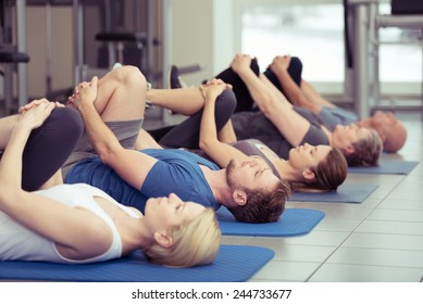 Diverse group of people in a gym class lying in a receding row on mats doing leg flexes in a health and fitness concept - Powered by Shutterstock