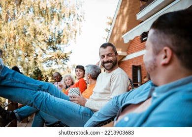 Diverse group of People hanging out, chatting and enjoying sunny autumn day in house porch. Happy Friends sitting outside in home patio, drinking mug - Powered by Shutterstock