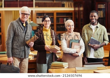 Diverse group of people holding books in classic library and looking at camera