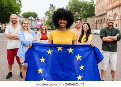 Diverse group of people holding European Union Flag while smiling at the camera standing together outdoors - Powered by Shutterstock