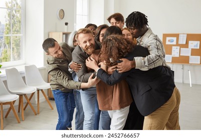 Diverse group of people in an office comes together in a embrace, symbolizing support, unity, and a welcome. Each individual contributes to the strength of the team, forming a symbol of teamwork. - Powered by Shutterstock